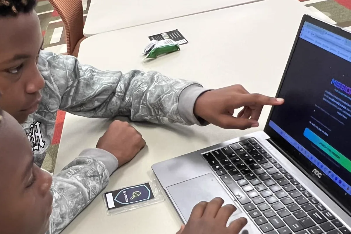 Two students at a laptop during a JAB AI coding workshop, one pointing at the screen they are building