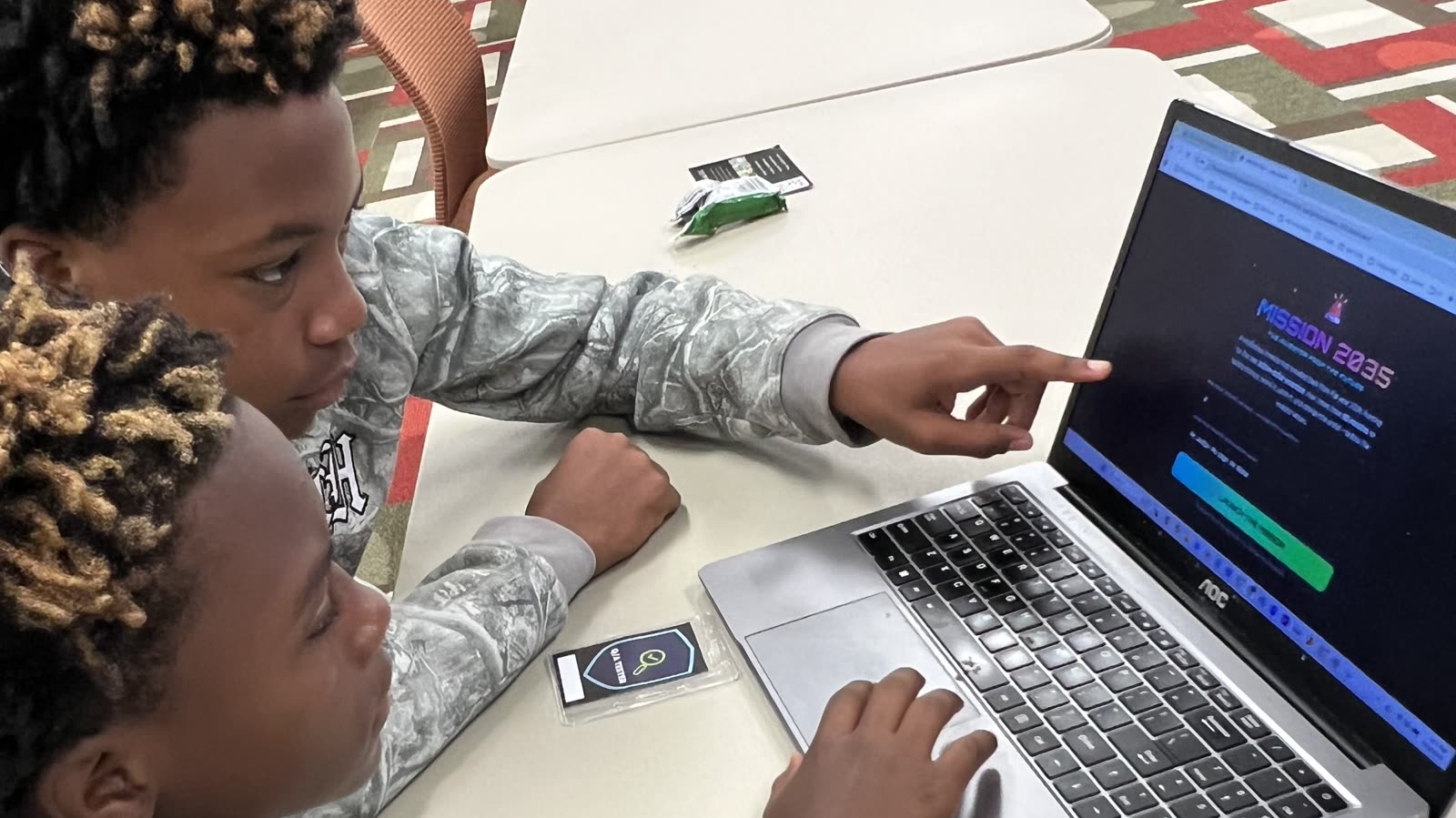 Two students at a laptop during a JAB AI coding workshop, one pointing at the screen